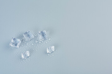 Ice cubes on a gray background in water droplets, free space