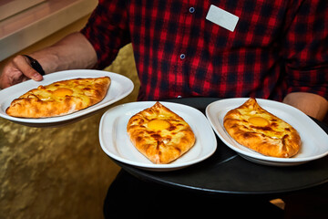 The waiter is holding plates with Ajarian traditional flatbread khachapuri or hachapuri with cheese, egg and butter on a plate