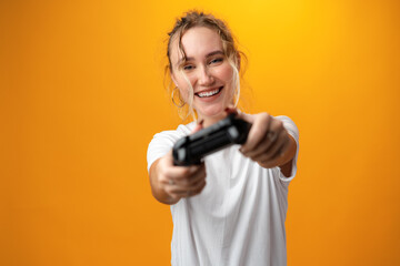 Fototapeta na wymiar Young woman plays games with joystick against yellow background