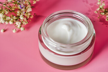 Glass jar and white cap with body cream on pink background. Cosmetic product for skin care. Transparent jar with face