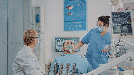 Dentistry nurse doing anesthesia with oxygen mask on patient, preparing to do drill procedure to...