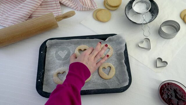 Woman baking linzer heart shaped biscuits. Picking up biscuits from a baking tray leaving behind heart shape in icing sugar. Valentine's day baking gift concept with white background. Real time motion