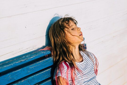 Outdoor summer portrait of cute hait colored girl suffering summer heat. The school girl sits and is exhausted from the heat after outdoor activity while hot sunny day. 