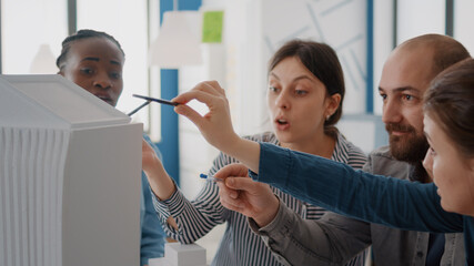 Obraz premium Close up of workmates analyzing building model and maquette on table to design construction. Group of diverse colleagues working on architecture project for structure and development.