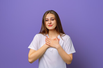 Portrait of brunette young woman keeps hands on chest, expresses sympathy. Kind hearted friendly nice girl shows kindness, wearing blank white t-shirt