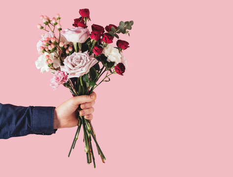 Male hand holding a beautiful bouquet on a pink background. Birthday, mother's or valentine's day gift. Copy space
