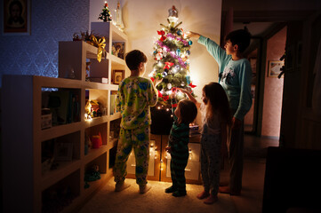 Kids looking on Christmas tree with shining garlands on evening home.