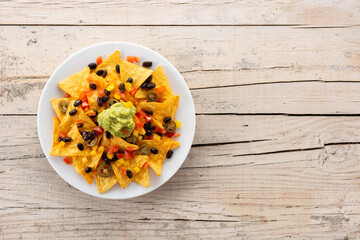 Mexican nachos tortilla chips with black beans, guacamole, tomato and jalapeno on wooden table. Top view. Copy space