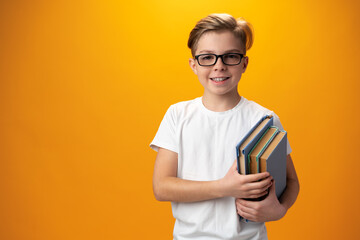 Little schoolboy holding a book against yellow background