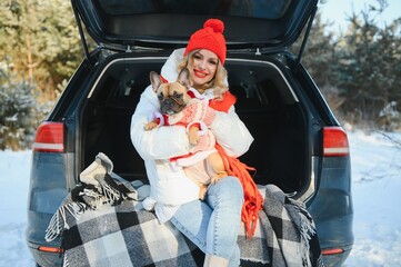 Young woman with dog sitting in open trunk of car. winter forest vacation.