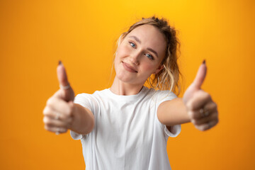 Young teen woman showing thumbs up sign against yellow background