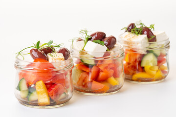Vegetable salad with cheese in glass jars. Greek salad. Salads to take away. On a white background....