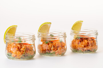 Raw salmon tartare in glass jars with a slice of lime. On a white background. Isolate