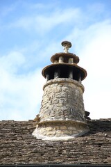 Traditional round multi-storey chimney built of pale yellow local limestone and roof tiles atop an ancient looking terracotta roof in a village in the Spanish Pyrenees