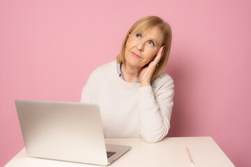 Attractive senior female sitting isolated on desk with computer.