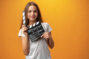 Smiling teen girl holding clapper board against yellow background