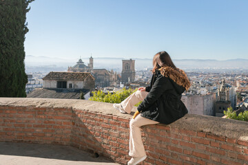 Granada old town and the Cathedral. Woman is sitting on the wall and seeing the Granada's views. It's a sunny day in Granada, Andalusia, Spain.