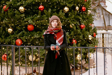 Christmas. Woman in winter clothes with gifts at the Christmas market. Girl outdoors. 