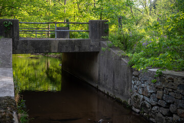 Bridge over a stone canal with green woods reflected in water