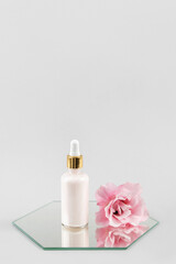 One glass dropper bottle with serum, essential oil or other cosmetic product and beautiful pink flowers on mirror on grey background. Natural Organic Spa Cosmetic Beauty concept. Copy space