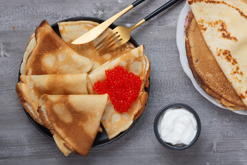 Stack of russian thin pancakes blini with red caviar and fresh sour cream