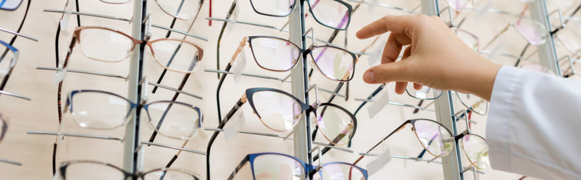 cropped view of oculist taking eyeglasses in optics store, banner.