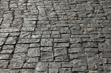 Old street paving stone of rough granite stone of irregular shape close-up. Texture of the stone roadway, background. View of the remains of the old laying of the ancient street. Blurred background