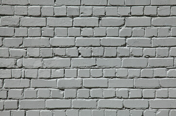 Grey brick wall texture, background. Surface in gray old-style color. Uneven brickwork and wall, painted with white water-based paint. An old rough whitewashed wall surface in backlight