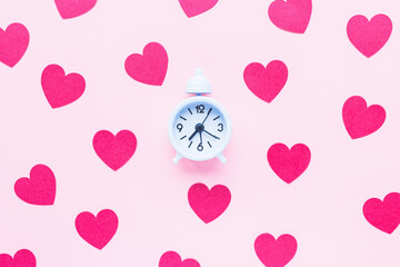 Valentines Day background with small white alarm clock and red hearts on pink. Love, dating, dinner planning and shopping gifts concept. Top view