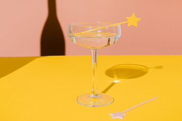 Champagne coupe glass with a star cake pick topper and a sharp champagne shadow on yellow and pink vivid background. Minimal modern still life. Party celebration concept. Luxury concept.