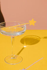 Champagne coupe glass with a star cake pick topper and a sharp champagne shadow on yellow and pink vivid background. Minimal modern still life. Party celebration concept. Luxury concept.