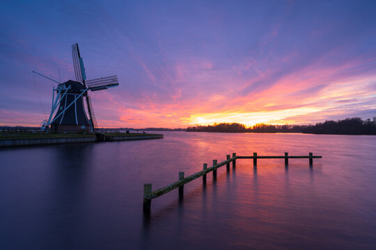 Dutch windmill at a lake during windy and colourful sunset.