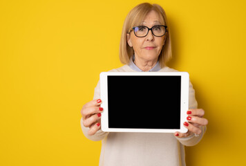 Photo portrait of senior woman showing tablet screen with copy space isolated on yellow background