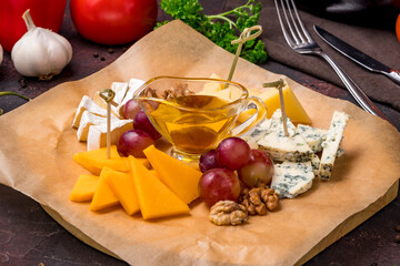 Cheese plate with different cheeses, honey and grapes, italian food on dark table