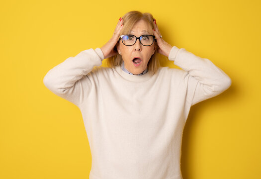 Elderly amazed woman in glasses open mouth gawp look at camera feels stunned isolated on yellow background