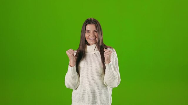 Joyful young woman saying yes and celebrating success with gesture in studio. Isolated over chroma key background. Victory and triumph concept.