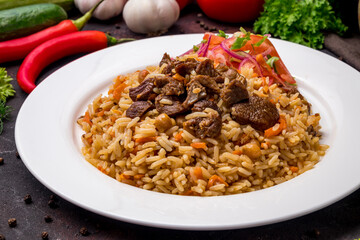 pilaf with beef and vegettables salad on white plate on dark table