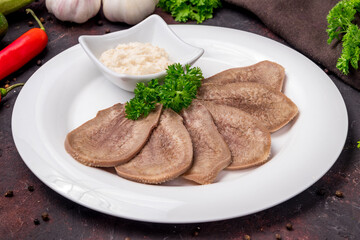 Beef tongue with horseradish on white plate on dark table