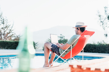 man sitting on beach chair by the swimming pool with a laptop alone