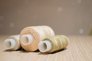 Three spools of beige thread on table on blurry