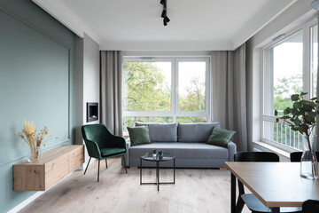 Modern living room in minimal interior with big window, sofa, armchair and green wall. Scandinavian concept for cozy room.