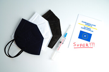 
Covid Green Pass with text "super", colored ffp2 mask, hand sanitizer, and syringe labeled "vaccine booster dose" on a white surface. Introduction of the super green pass and third dose of the vaccin