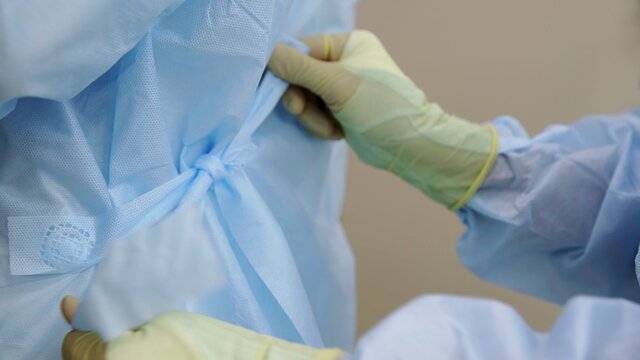 Close-up of professional doctors in uniform, wearing dressing gowns with ties at the back, preparing for surgery. Medicine
