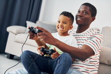 Playing video games. African american father with his young son at home