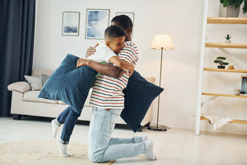 Holding pillows. African american father with his young son at home