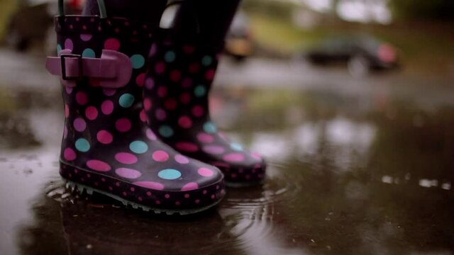 Unrecognizable girl jumping in a pool of water during rainy day with waterproof boots, close up of the feet with selective focus