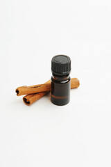 Small dark glass bottle and cinnamon sticks on white. Essential oil or extract. Cosmetic or food concept