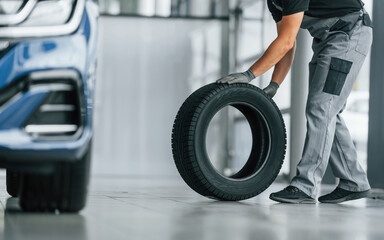 Tire on the floor. Man in uniform is working in the autosalon at daytime