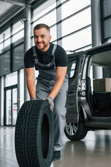 Plakat Brand new tire. Man in uniform is working in the autosalon at daytime