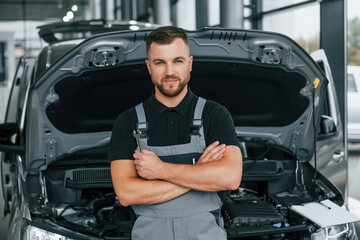 Arms crossed. Man in uniform is working in the autosalon at daytime